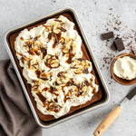Finished dessert in a Nordic Ware aluminum baking pan on a textured surface with utensils and chocolate pieces