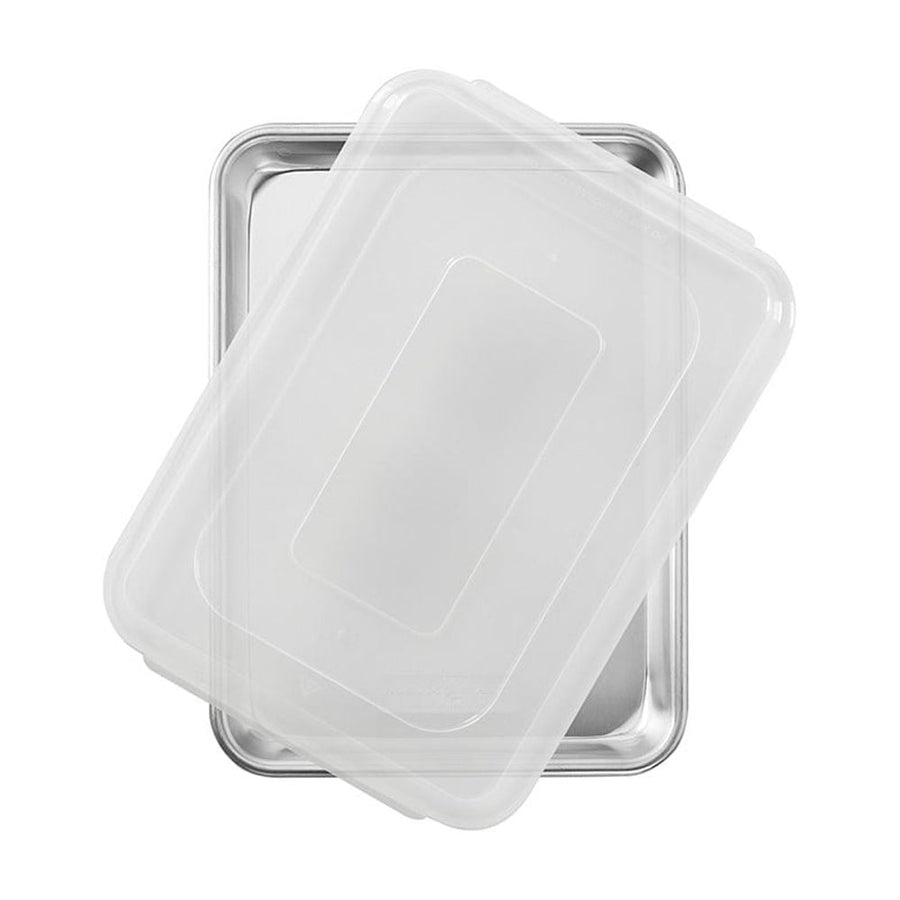 Overhead photo of a rectangular aluminum quarter sheet pan with a translucent plastic lid partially covering it on a white background.
