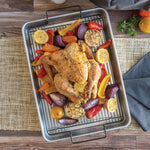 Top-down view of a roasted chicken and vegetables on a crisping rack inside an aluminum roasting pan on a placemat