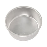 Angled close-up of a silver Nordic Ware round cake pan interior showing the rolled rim and embossed logo on the base
