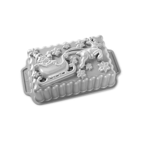 Nordic Ware cast-aluminum loaf pan with raised Santa-in-sleigh and reindeer holiday design on metallic surface