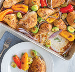 Close-up of roasted chicken pieces and vegetables in an aluminum sheet pan used for baking or roasting