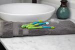 Three blue-and-green baby toothbrushes and a clear fingertip brush resting on a grey towel beside a bathroom sink