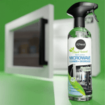 Nuvera microwave cleaner bottle staged in front of a microwave on a green background, product lifestyle view