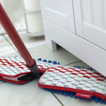 O-Cedar mop head attached to handle cleaning along baseboard and cabinet edge on tile floor