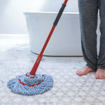 Lifestyle shot of O-Cedar mop with red handle and blue-and-white microfiber refill on tiled bathroom floor near bare feet