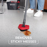O-Cedar red scrub head on a pole scrubbing a sticky spill on a hard floor with EasyWring bucket and person’s lower legs in background.