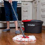 Person mopping a kitchen floor with an O-Cedar spin mop and the O-Cedar bucket visible in the background