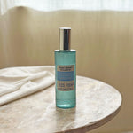 Better Homes & Gardens Oceanside Flannel teal spray bottle placed on a round marble table with folded linen and soft curtain backdrop