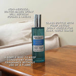 Styled lifestyle image of Oceanside Flannel spray bottle on a wooden surface with overlaid text calling out non-aerosol water-based spray and pump action nozzle