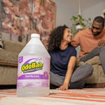 OdoBan lavender disinfectant jug placed on a rug in a living-room setting with two people blurred in the background.