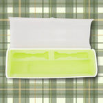 Open translucent travel case showing lime-green molded interior with two toothbrush-shaped slots on a plaid background.