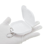 Open compact white plastic retainer case resting on a gloved hand with attached metal carabiner ring