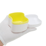 Open white plastic denture case with a yellow interior held in a gloved hand, showing internal drainage slots