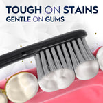 Close-up of a black toothbrush head brushing teeth with text 'Tough on stains gentle on gums' in background