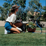 Gardener kneeling beside planters as a blue flexible misting hose emits mist nearby