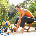 Woman potting plants on a patio while a blue Orbit Cobra misting hose stands nearby spraying mist