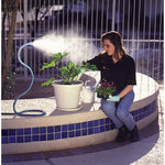 Outdoor scene of a blue Orbit Cobra misting hose spraying a fine mist near potted plants