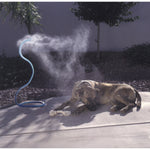 Blue flexible misting hose producing visible mist while a dog lies on a sunlit patio