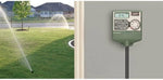 Orbit Easy Dial sprinkler timer mounted on a wall beside a green lawn with sprinklers