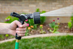 Orbit 6-pattern lever-control hose nozzle spraying a fine stream in a garden with flowers in background