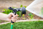Orbit 6-pattern lever-control hose nozzle spraying water, held over a lawn with flowerbed background