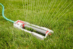 Orbit oscillating lawn sprinkler connected to a hose, spraying water across a grassy yard