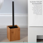Lifestyle photo of a black-handled toilet brush standing in a ribbed bamboo square holder beside a white bathroom vanity.
