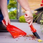 Person sweeping dried leaves and petals with a red whisk broom into a matching dustpan outdoors