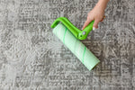 Close-up overhead view of a hand rolling a large green Evercare lint roller across patterned carpet