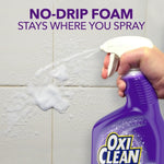 Hand spraying clinging white foam from a purple OxiClean bottle onto tiled grout with text
