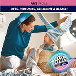 Woman and child playing among laundry in a bright room with OxiClean Baby logo and a banner claiming free from dyes, perfumes, chlorine and bleach.