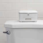 White OXO wipe dispenser placed on top of a toilet tank with tiled wall background