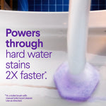 Action shot of a purple scrubbing pad foaming in a toilet bowl next to purple text claiming it powers through hard water stains faster.