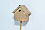 Front-facing view of a small painted metal birdhouse on a stake against a light fabric backdrop