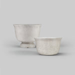 Two light-gray gypsum planters displayed on a neutral background, one taller urn and one low bowl