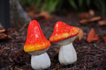 Pair of orange and yellow-tipped mushroom garden decorations arranged on mulch with blurred foliage background.