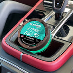 Turquoise gel air freshener with black vented lid and ‘Ultimate Gel 90 Tsunami’ label placed in a car center console cup well.