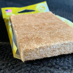 Close-up of a brown fibrous air freshener pad partially pulled from a yellow-green Paradise Air Super Organic pouch.