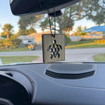 Square wooden Paradise Air hanging air freshener with a turtle laser-cut design suspended from a car mirror with neighborhood background