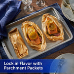 Baking sheet lined with unbleached parchment packets containing salmon topped with lemon slices on a table setting