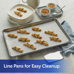Tray of crescent-shaped pastries on parchment-lined baking sheet with plates and bowls in background