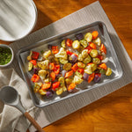 Roasted mixed vegetables on a parchment-lined sheet pan set on a table with serving bowl and spoon