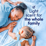 Parent and baby on a blue bedspread with text 'Light scent for the whole family' promoting Downy Light Ocean Mist