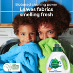 Parent and child holding fresh towels in front of a washing machine with Seventh Generation bottle visible