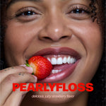 Close-up lifestyle shot of a smiling person biting a ripe strawberry with PEARLYFLOSS logo and flavor text overlaid.