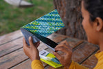 Hands peeling backing off a corrugated FlyPad adhesive trap with package visible on the table behind