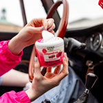 Hands peeling the vented lid off a Citrus Magic Dragonfruit car solid air freshener inside a vehicle