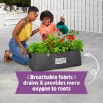 Two people kneeling and watering plants growing in a gray Back to the Roots fabric raised bed on a paved surface.
