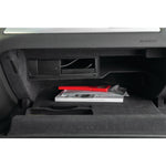Red compact ice scraper in its packaging stored inside a vehicle glovebox resting on top of a manual.